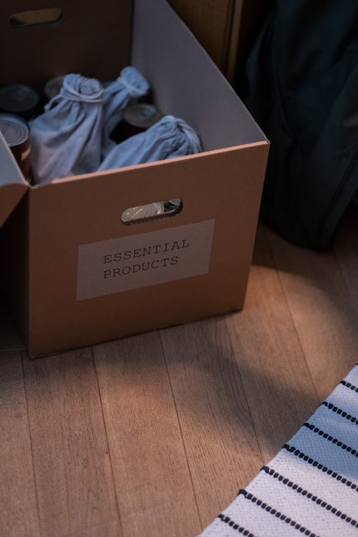 services-02 Cardboard box labeled 'Essential Products' filled with goods on wooden floor.